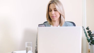 Ofiste çalışan kadın muhasebeci akıllı telefonlara bakıyor, mesajları okuyor. İş yerinde dizüstü bilgisayarı olan kadın finans danışmanı.