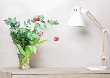 Laleli bahar buketi ve ahşap bir masada cam vazoda yeşil yapraklar ve beyaz İskandinav tarzı lamba. ürün yerleştirme için kopyalama alanı