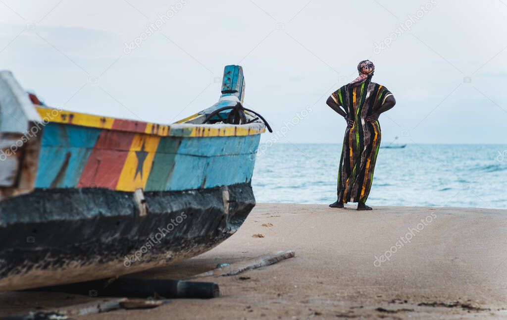 African woman in long suit standing by the shore and looking out over the sea in Keta Ghana West Africa