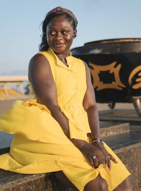 African woman sitting with yellow dress at sunset in Independence Arch Accra Ghana West Africa October 2021