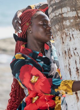Afrikalı bir kadın Accra Gana sahilinin gölgesinde palmiye ağacına sarılıyor.