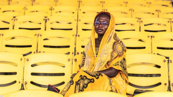 African woman in beautiful yellow suit sitting alone on an empty audience stand in Accra Ghana, West Africa