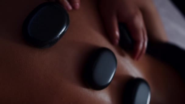 Mujer joven relajándose en el salón de spa con masaje corporal de piedra caliente. — Vídeos de Stock