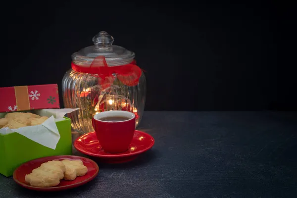 コピースペースフロントビューで暗い背景に紅茶とクリスマスライトとクリスマスのショートブレッドギフト — ストック写真