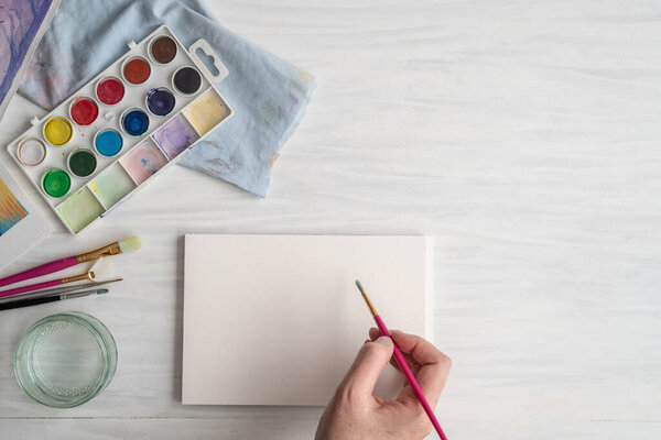 Человек, готовящийся нарисовать акварель красками, кисточками и чистой бумагой на столе с копировальным пространством сверху