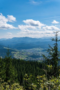 Sıcak, güneşli bir günde, dinamik beyaz bulutlarda dağların, köyün ve yeşil ormanın güzel manzarası.