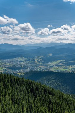 Sıcak, güneşli bir günde, dinamik beyaz bulutlarda dağların, köyün ve yeşil ormanın güzel manzarası.