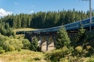 Dağlardaki büyük, eski bir su kemeri köprüsünde giden bir tren.