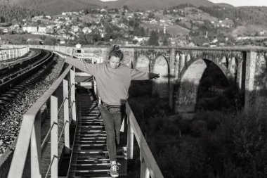 Genç bir kadın dağlarda bir tren istasyonunda eğleniyor.