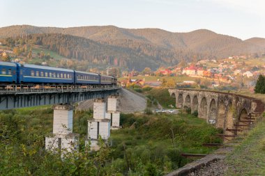 Dağlardaki büyük, eski bir su kemeri köprüsünde giden bir tren.