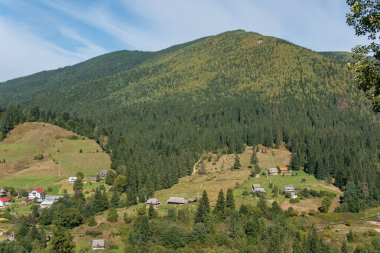 Güneşli bir günde tepelerde, dağlarda, yeşil ormanlarda ve küçük bir köydeki evlerde hava manzarası