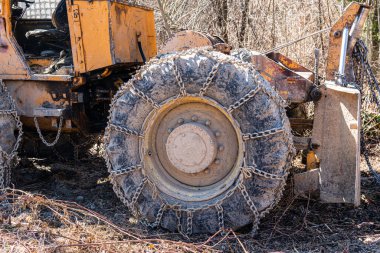 Güneşli bir günde zincirlenmiş tekerlekleri ve kovası olan büyük bir traktör.