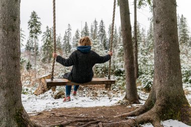 Poland, Rabka-Zdroj   April 10, 2022: A pregnant woman is swinging outdoors in winter with amazing view on the forest
