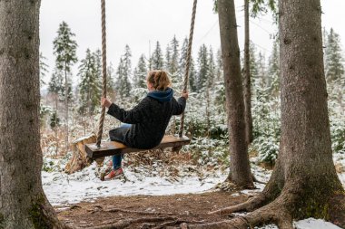 Poland, Rabka-Zdroj   April 10, 2022: A pregnant woman is swinging outdoors in winter with amazing view on the forest
