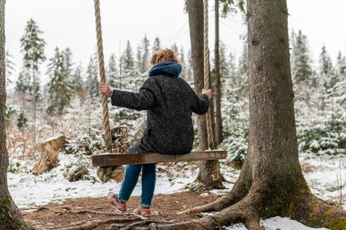 Poland, Rabka-Zdroj   April 10, 2022: A pregnant woman is swinging outdoors in winter with amazing view on the forest