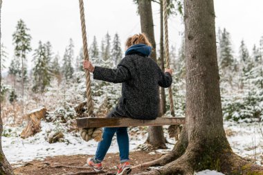 Poland, Rabka-Zdroj   April 10, 2022: A pregnant woman is swinging outdoors in winter with amazing view on the forest