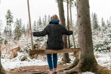 Poland, Rabka-Zdroj   April 10, 2022: A pregnant woman is swinging outdoors in winter with amazing view on the forest