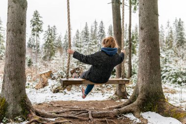 Poland, Rabka-Zdroj   April 10, 2022: A pregnant woman is swinging outdoors in winter with amazing view on the forest