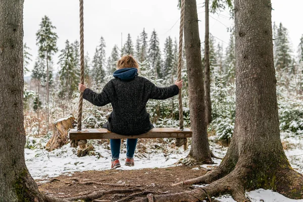 Poland, Rabka-Zdroj   April 10, 2022: A pregnant woman is swinging outdoors in winter with amazing view on the forest