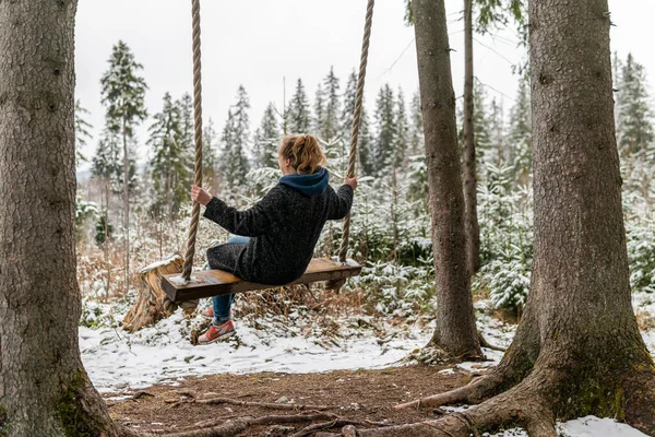 Poland, Rabka-Zdroj   April 10, 2022: A pregnant woman is swinging outdoors in winter with amazing view on the forest