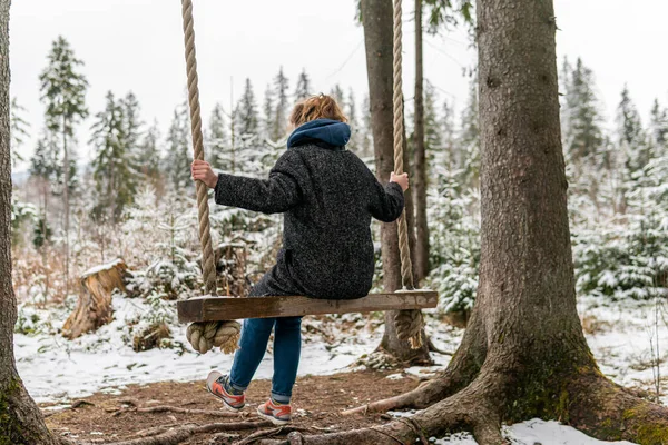 Poland, Rabka-Zdroj   April 10, 2022: A pregnant woman is swinging outdoors in winter with amazing view on the forest