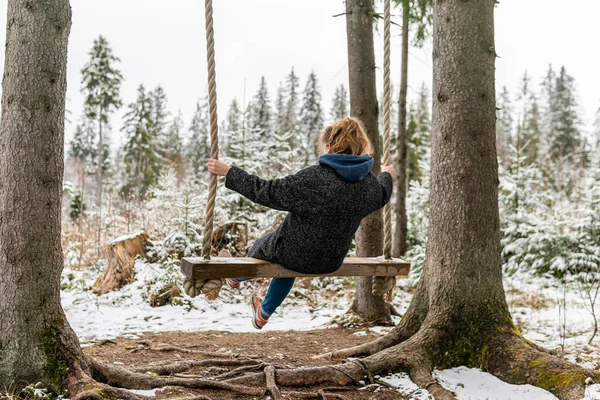 Poland, Rabka-Zdroj   April 10, 2022: A pregnant woman is swinging outdoors in winter with amazing view on the forest