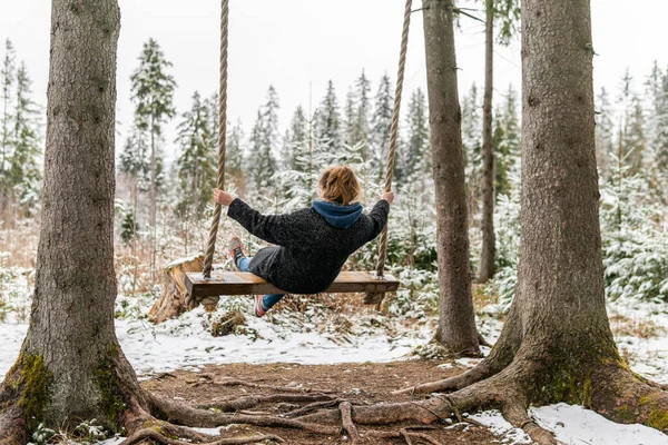 Poland, Rabka-Zdroj   April 10, 2022: A pregnant woman is swinging outdoors in winter with amazing view on the forest