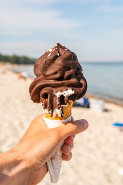 Keeping a big melting chocolate waffle corn ice-cream in a hand on a sunny beach