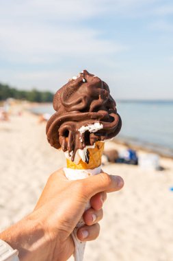 Keeping a big melting chocolate waffle corn ice-cream in a hand on a sunny beach