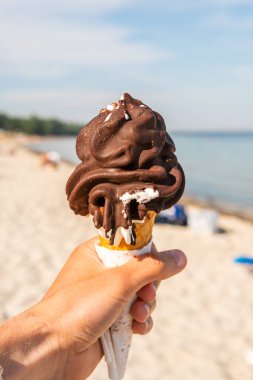 Keeping a big melting chocolate waffle corn ice-cream in a hand on a sunny beach