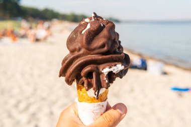 Keeping a big melting chocolate waffle corn ice-cream in a hand on a sunny beach