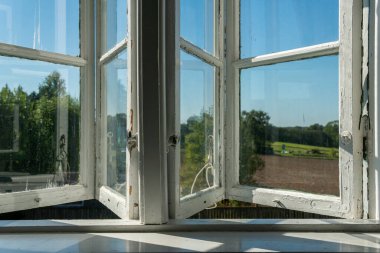 Köyün açık penceresinden bak. Mavi gökyüzü ve yeşil tarla manzaralı beyaz eski ahşap pencereler. İlgisizliğin, özgürlüğün, yaz atmosferinin sembolü. Tatil evi, yazlık ev, hafta sonu kulübesi.. 