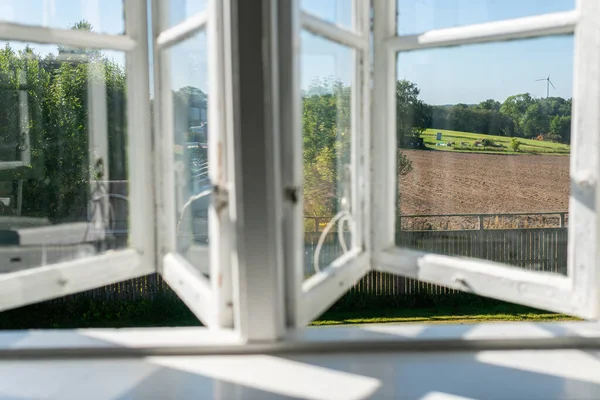 View from open window in the village. White old wooden windows with view on blue sky and green field. Symbol of insouciance, freedom, summer atmosphere. Holiday house, summer cottage, weekend cottage.