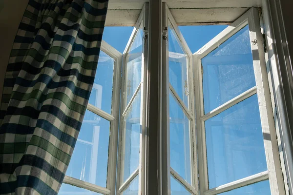 View from open window in the village. White old wooden windows with view on blue sky and green field. Symbol of insouciance, freedom, summer atmosphere. Holiday house, summer cottage, weekend cottage.