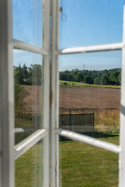 View from open window in the village. White old wooden windows with view on blue sky and green field. Symbol of insouciance, freedom, summer atmosphere. Holiday house, summer cottage, weekend cottage.