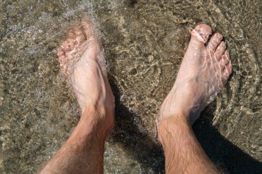 Sahilde ayakta duran ayaklar suyun kumları üzerinde, ferahlatıcı.