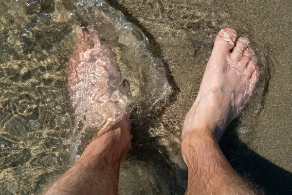 Feet standing on a beach on the sand in the water, refreshing.