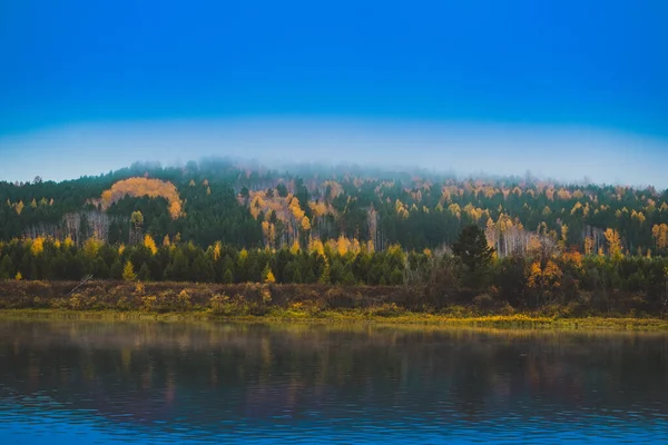 The landscape of the autumn riverbank with hills covered with dense forest of green and yellow leaves. Fog over the taiga river in Siberia. Lena River — Stock Photo, Image