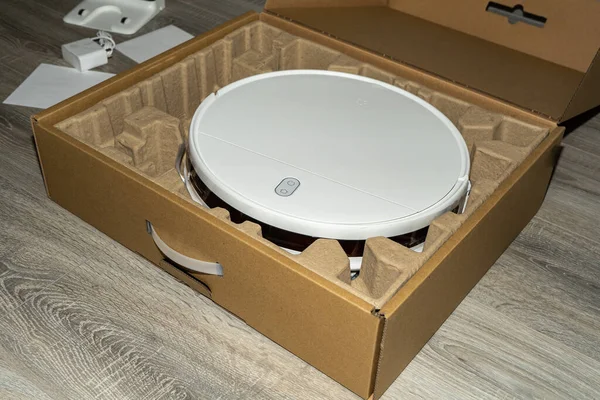unpacking of the robot vacuum cleaner. Robot vacuum cleaner in a cardboard box on wooden floor.