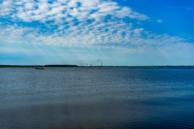 Su yüzeyinde dalgalanmalar ve mavi gökyüzünde bulutlar.