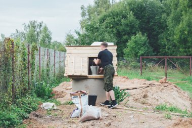 Bir adam bahçedeki bir kuyudan kovaya su topluyor.