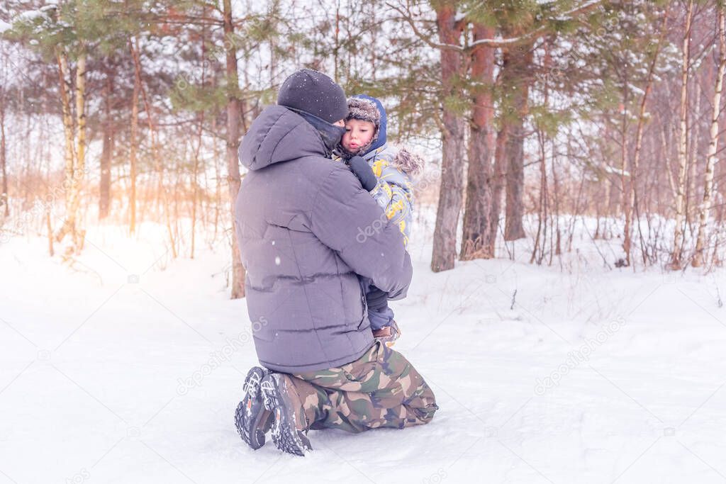 Dad holds and hugs his little son in a snowy forest or winter park. Concept of winter outdoors activities for family.