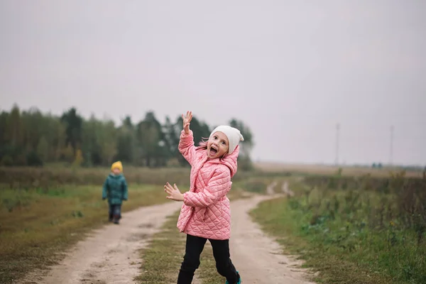 Little caucasian girl running in the field with her brother making funny faces.