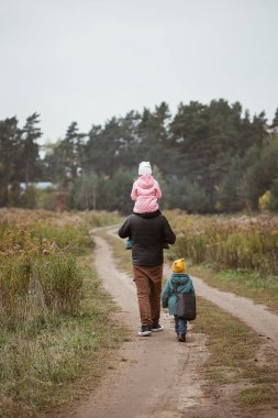 İki çocuklu mutlu bir aile sonbahar zamanı sahada yürüyor. Babam kızını omuzlarında taşıyor..