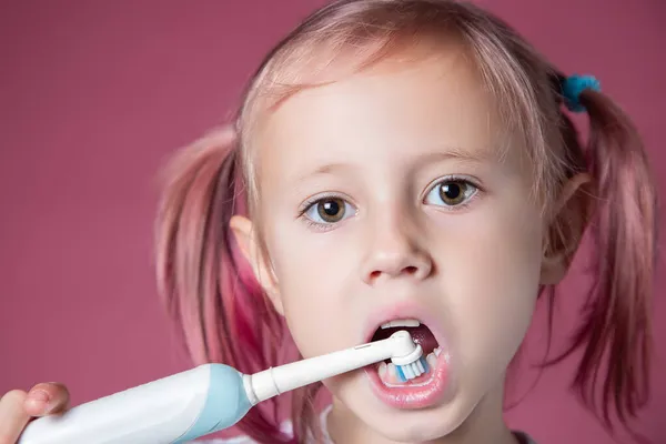 Sonriente niña caucásica limpiando sus dientes con un cepillo de dientes sónico eléctrico — Foto de Stock