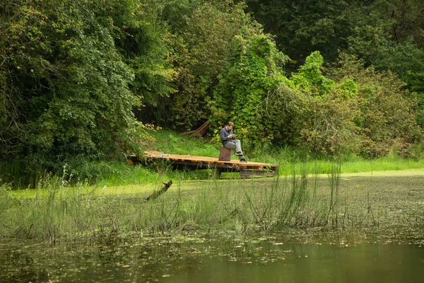 森の湖の上にある木製のボートドックに座っている男 — ストック写真