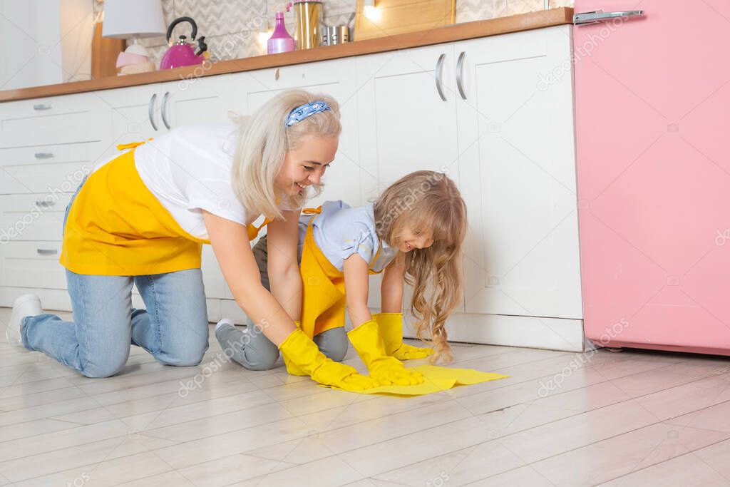 Caucasian Mom and cute little daughter wet cleaning the kitchen. Two female generations family together in kitchen.