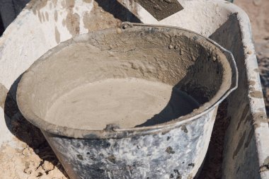 Bahçedeki yolda kum ve kuru çimentoyla dolu bir sepet duruyor.