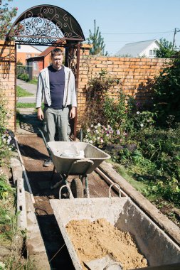 Bir adam çimento karışımına kum boşaltır bahçe yolu dökerek, bahçe arazisinde inşaat yapar.