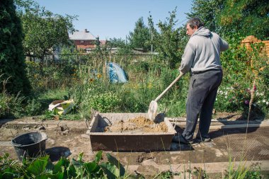 Yaşlı adam bahçe yolu için çimento yoğurur, bahçe inşaatı.